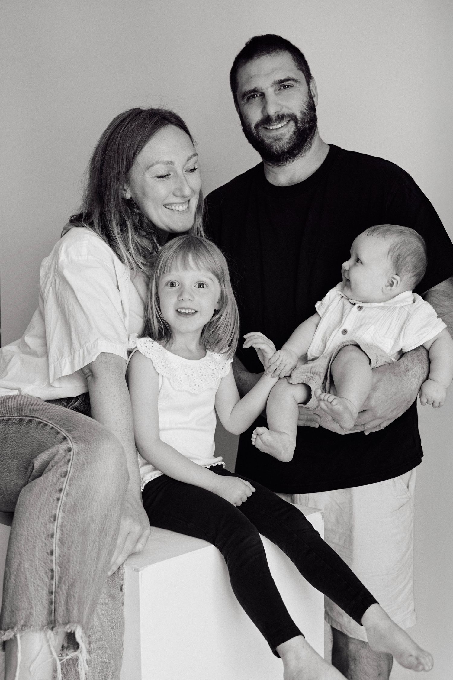 Black and white family portrait with parents and two young children, including a baby, posing together in a studio.