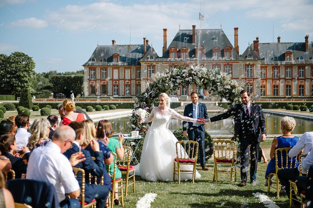Bride and groom celebrate with confetti toss in front of stunning French chateau wedding venue.