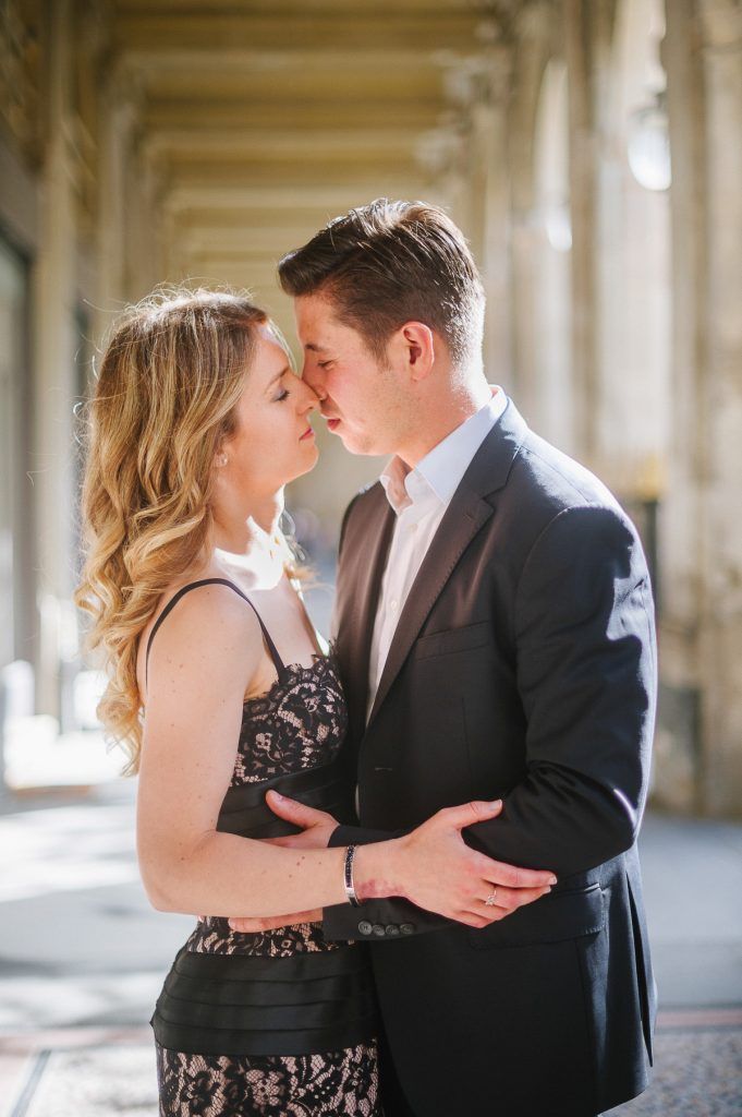 Close-up of an elegant couple sharing a romantic kiss under the arched columns of a classic Parisian building.
