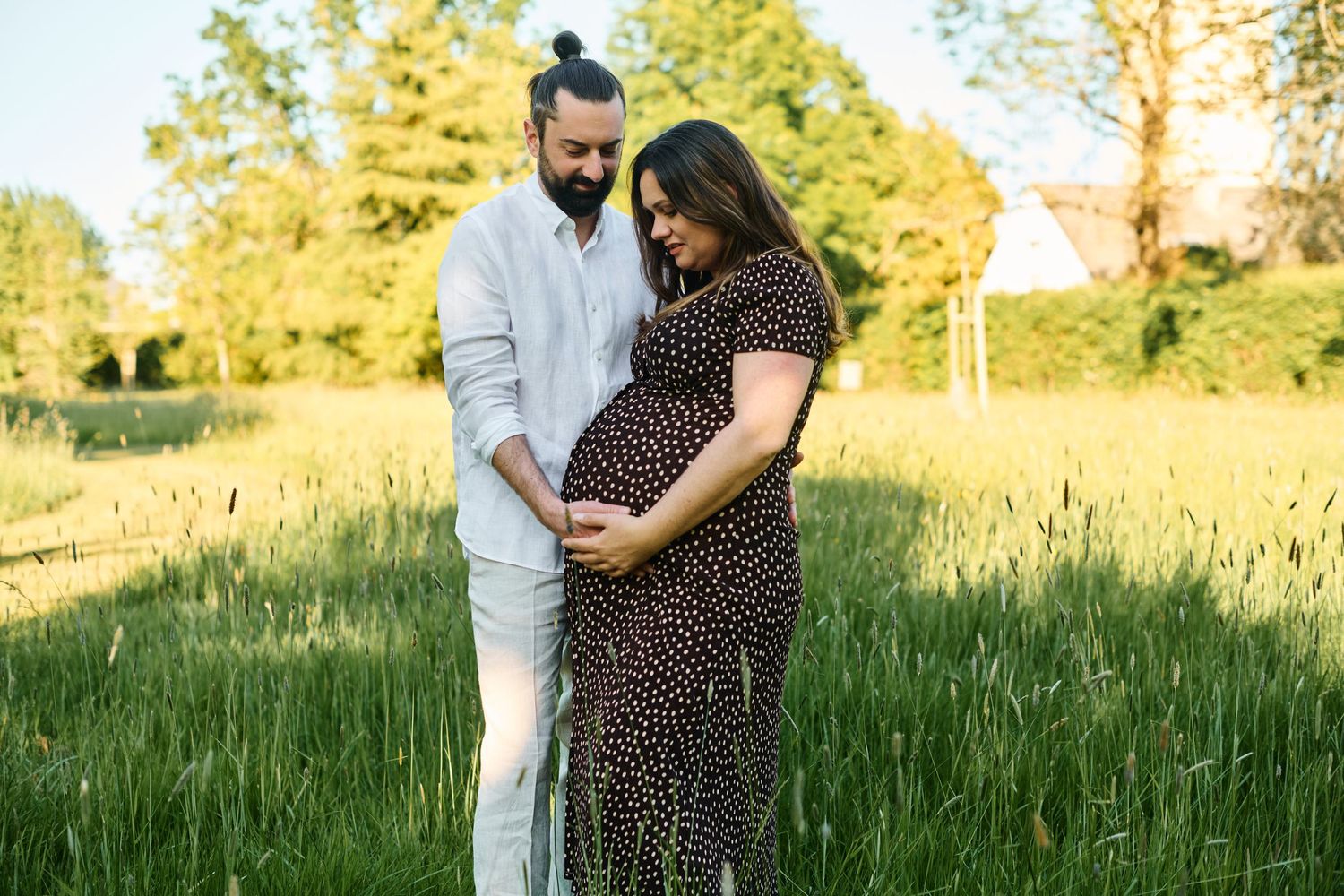 Couple standing in green field, man tenderly touching pregnant woman's belly at sunset.