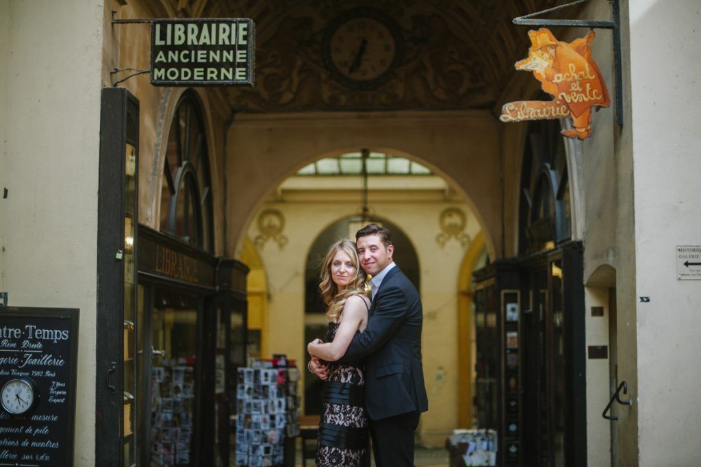 Couple embracing in front of Librairie Ancienne Moderne bookshop inside a charming Parisian covered passage.