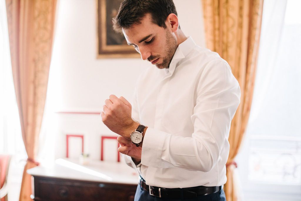 Groom in white shirt fastening cufflinks while getting ready for wedding ceremony.