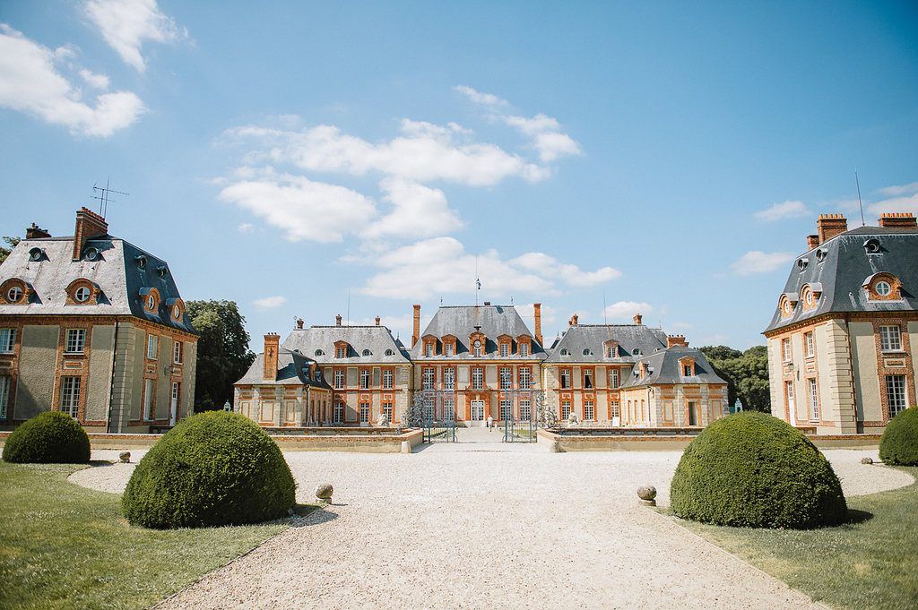 Grand French chateau with manicured topiary gardens under a bright blue sky on a sunny day.