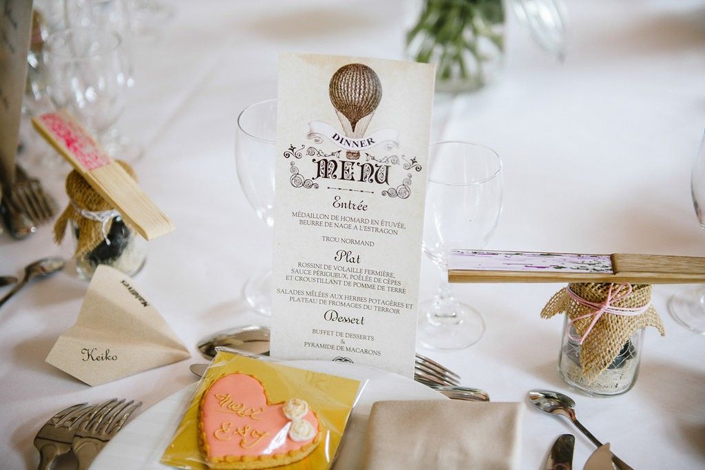 Decorative wedding menu card with hot air balloon design displayed on a white reception table.