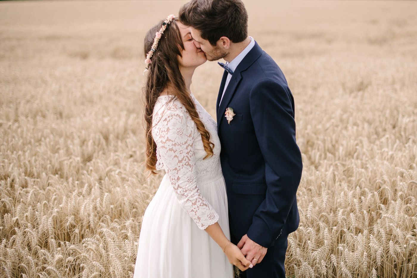 Bride and groom sharing a romantic kiss in a golden wheat field during their outdoor wedding.