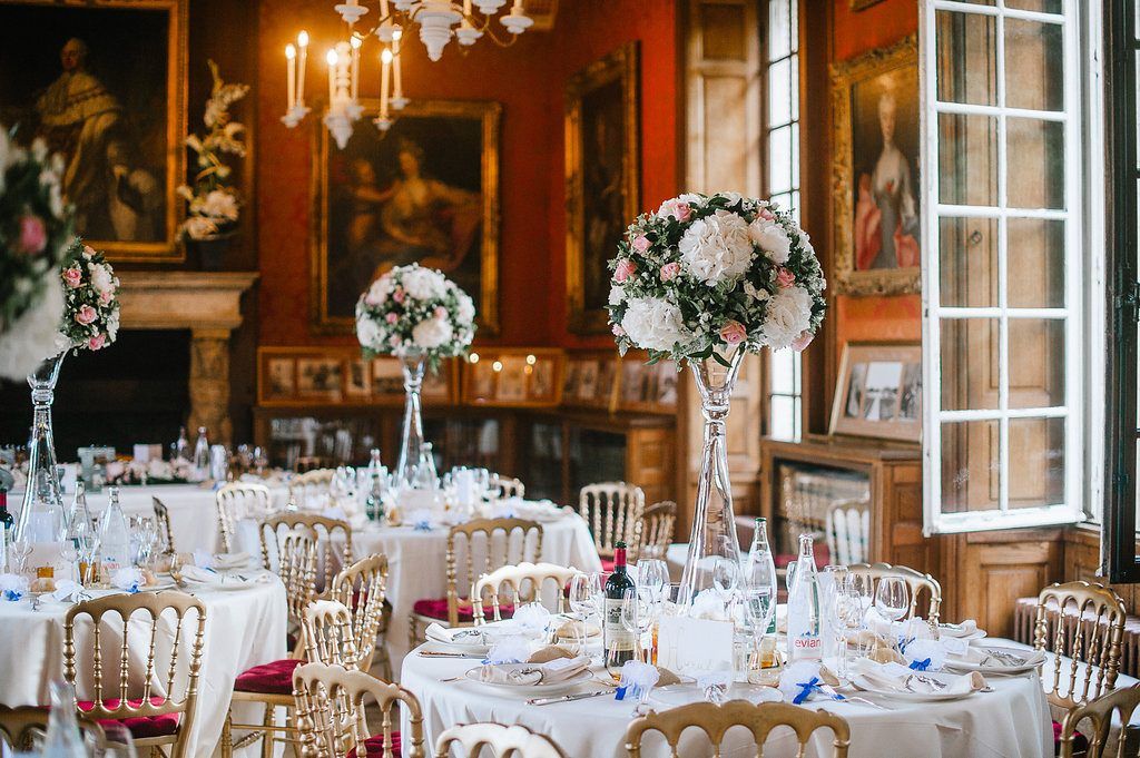 Luxurious wedding reception hall with tall floral centerpieces, candelabras, and gold Chiavari chairs.