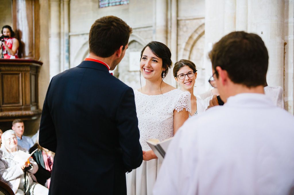 Smiling bride in lace wedding dress exchanges vows with groom during church wedding ceremony.
