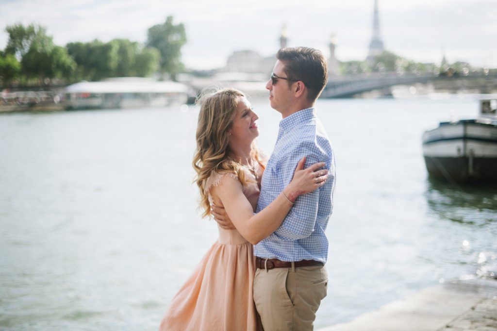 Happy couple gazing at each other while embracing along the Seine River in Paris.