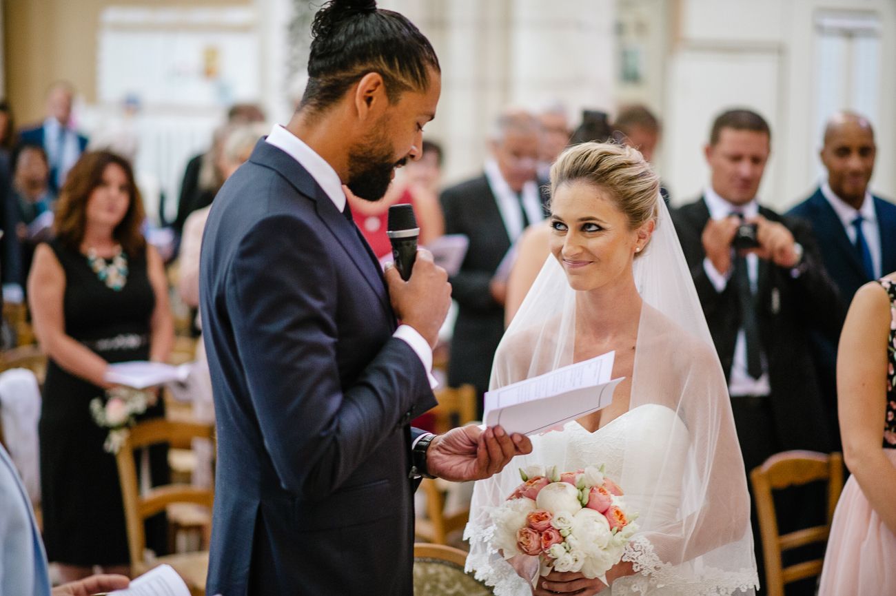 Groom reads vows to smiling bride holding bouquet at elegant wedding ceremony.