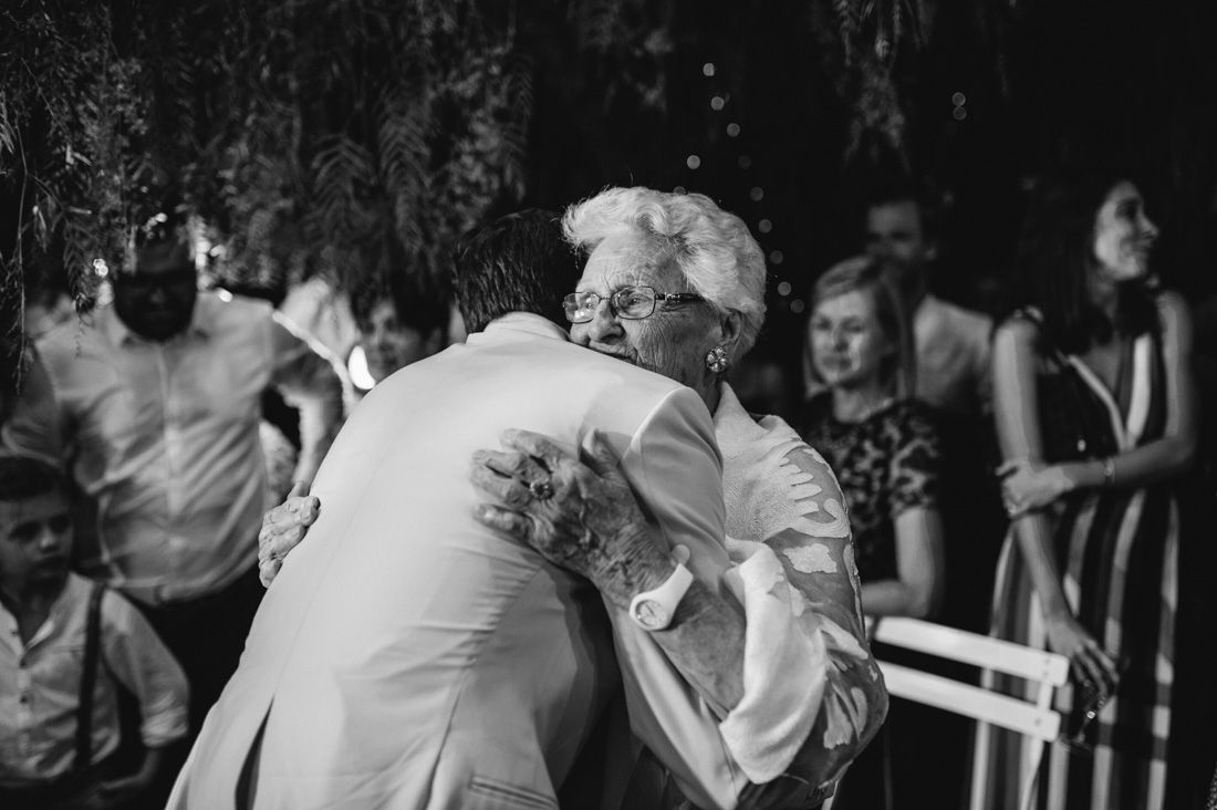 Elderly woman and groom share a heartfelt embrace at an outdoor wedding ceremony in black and white.