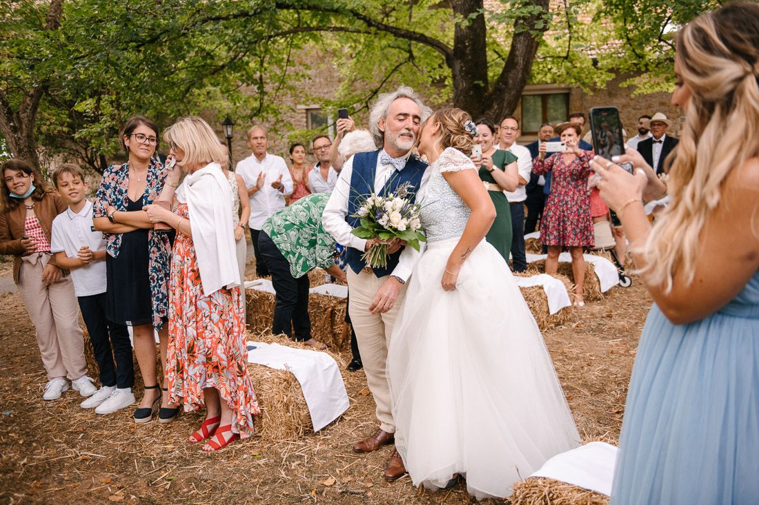 Bride and groom walk joyfully past cheering guests at rustic outdoor woodland wedding ceremony.