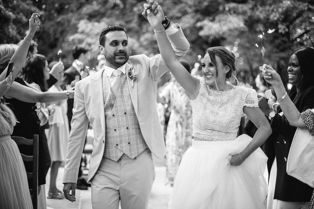 Black and white photo of newlyweds raising hands in celebration while walking through cheering wedding guests.
