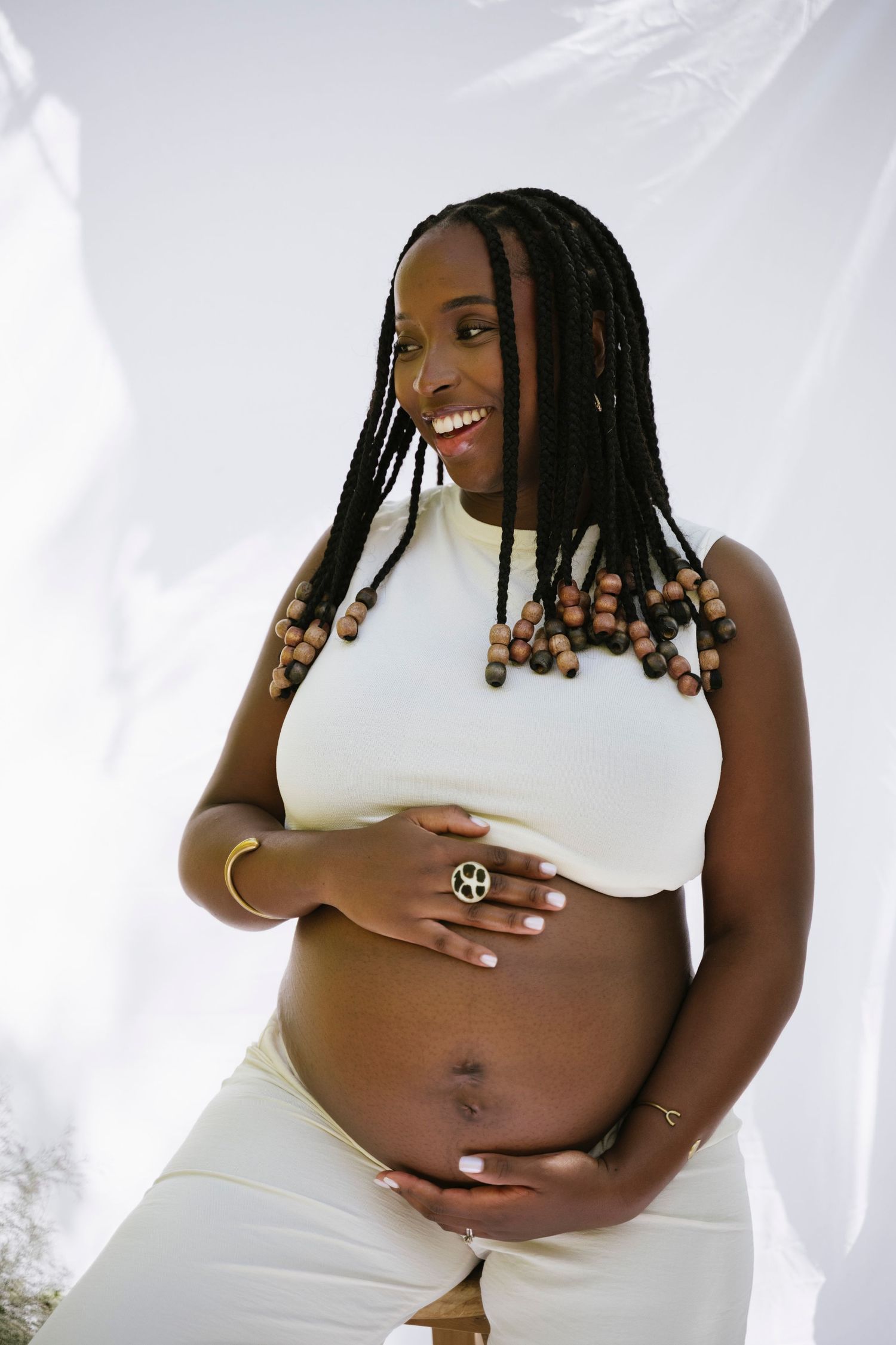 Smiling pregnant Black woman in white crop top cradling her baby bump outdoors.