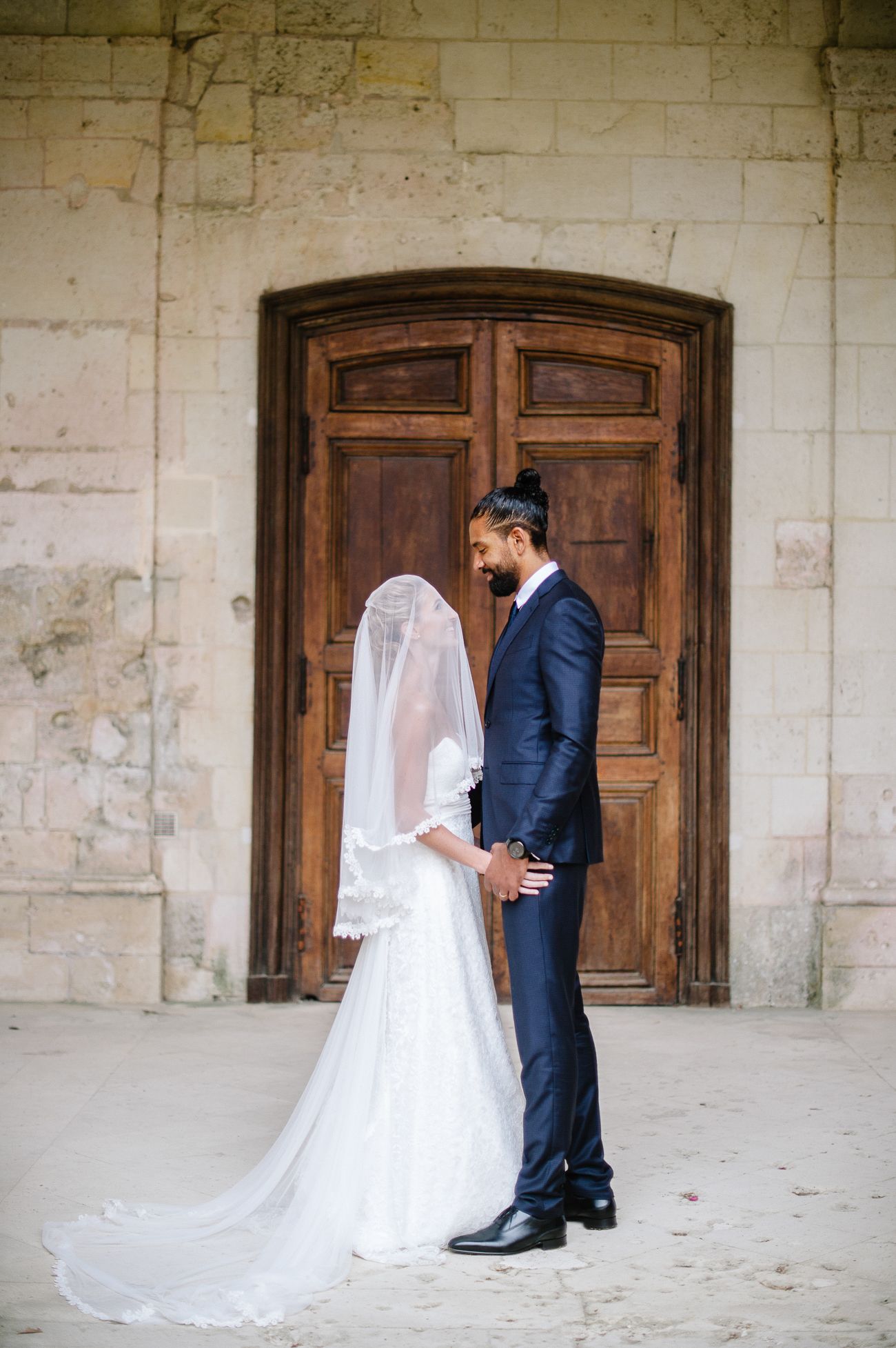 Bride and groom hold hands facing each other before rustic wooden doors on wedding day.