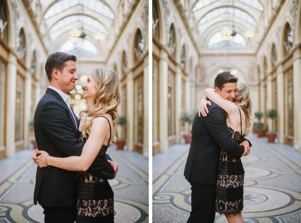 Happy couple embracing and smiling inside the beautiful arched gallery of Galerie Vivienne in Paris.