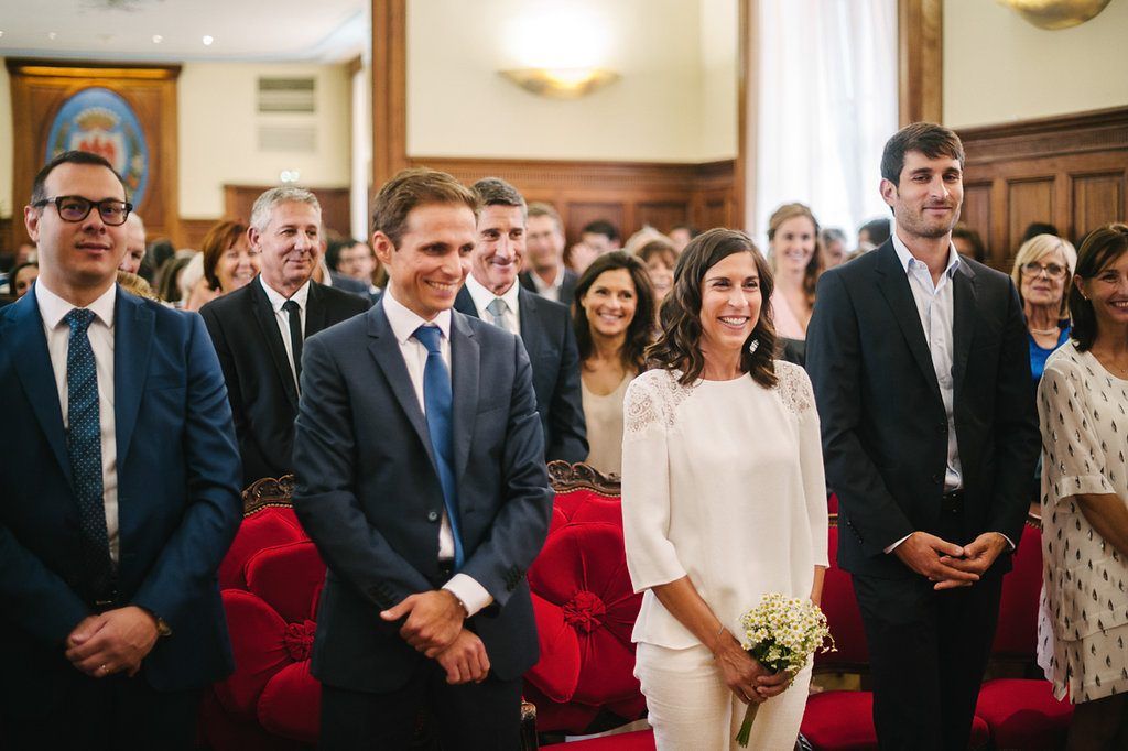 Bride and groom smile joyfully at civil wedding ceremony surrounded by applauding guests.