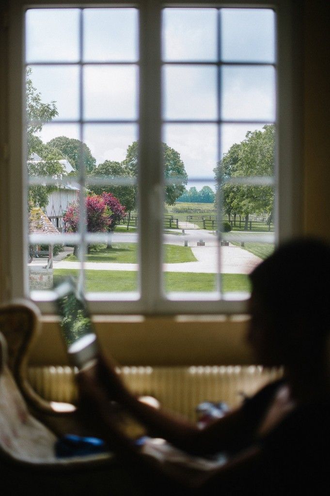 Person relaxing by a large window with a scenic view of a lush countryside estate.
