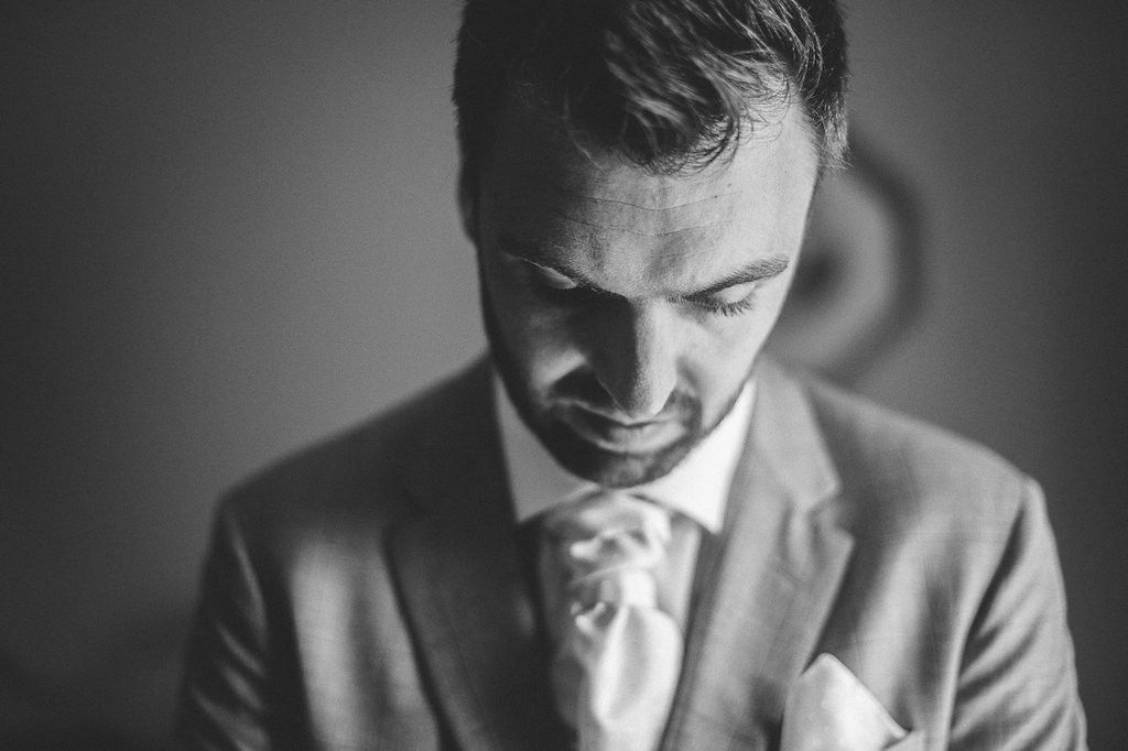 Black and white portrait of thoughtful bearded groom in gray suit with pink tie.