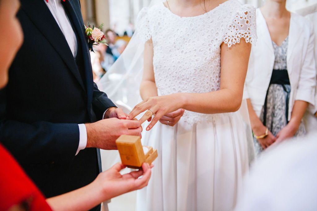 Bride places wedding ring on grooms finger during outdoor ring exchange wedding ceremony.