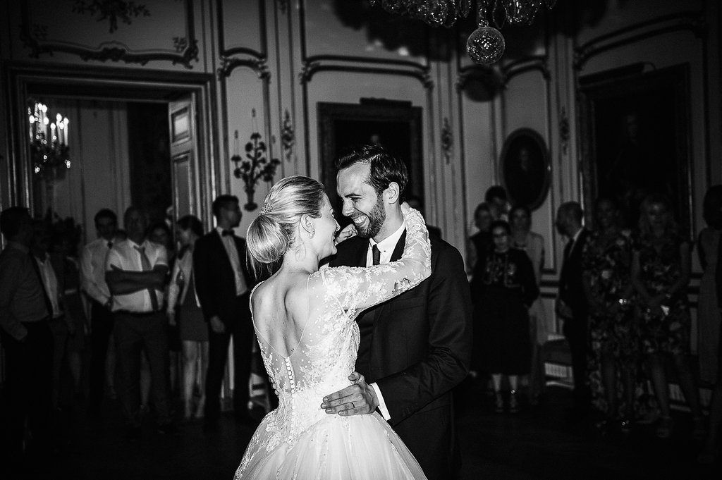Smiling groom holds bride close during first dance at elegant French chateau wedding reception in black and white.