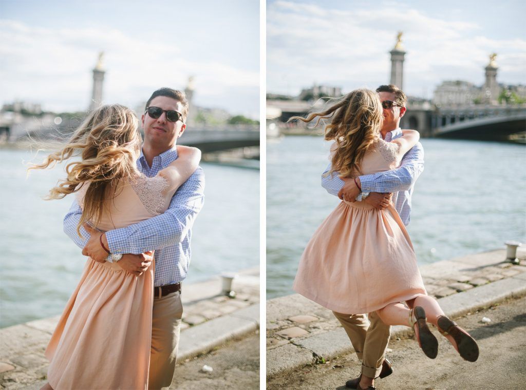 Joyful couple spinning and embracing by the Seine River with Pont Alexandre III behind them.