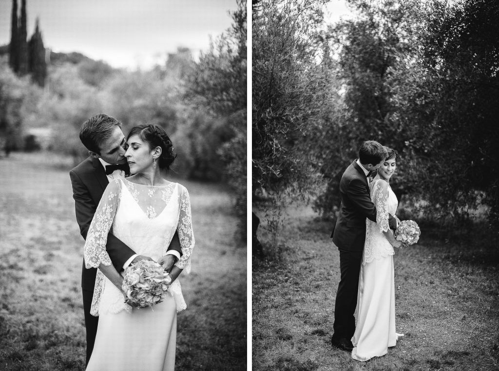 Black and white wedding couple embracing among olive trees in romantic outdoor portrait.