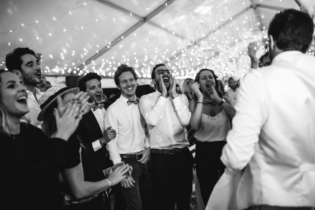 Joyful wedding guests laughing and celebrating on the dance floor inside a fairy light-filled reception tent.