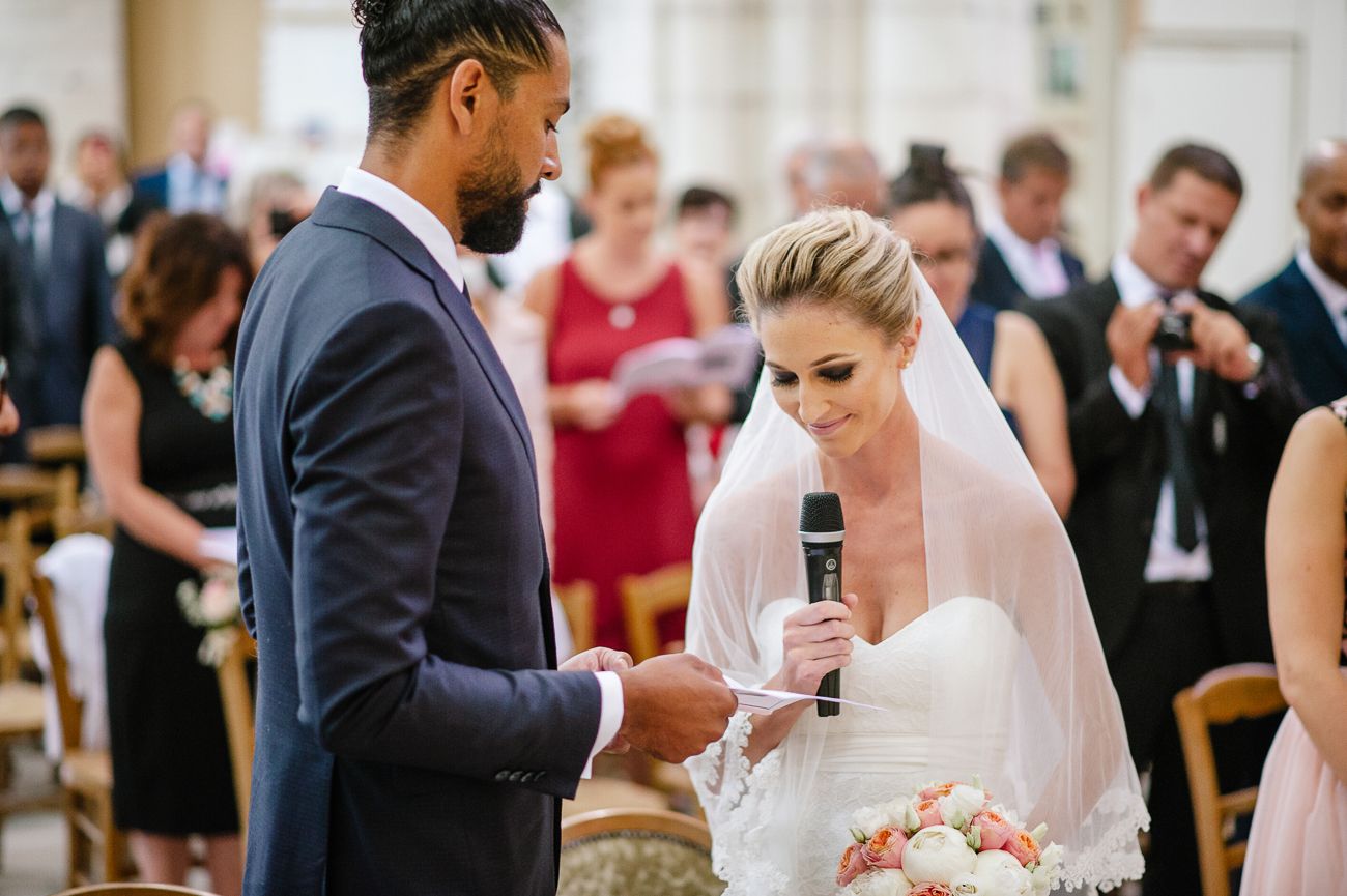 Bride reads wedding vows into microphone while groom holds her hand during elegant indoor wedding ceremony.