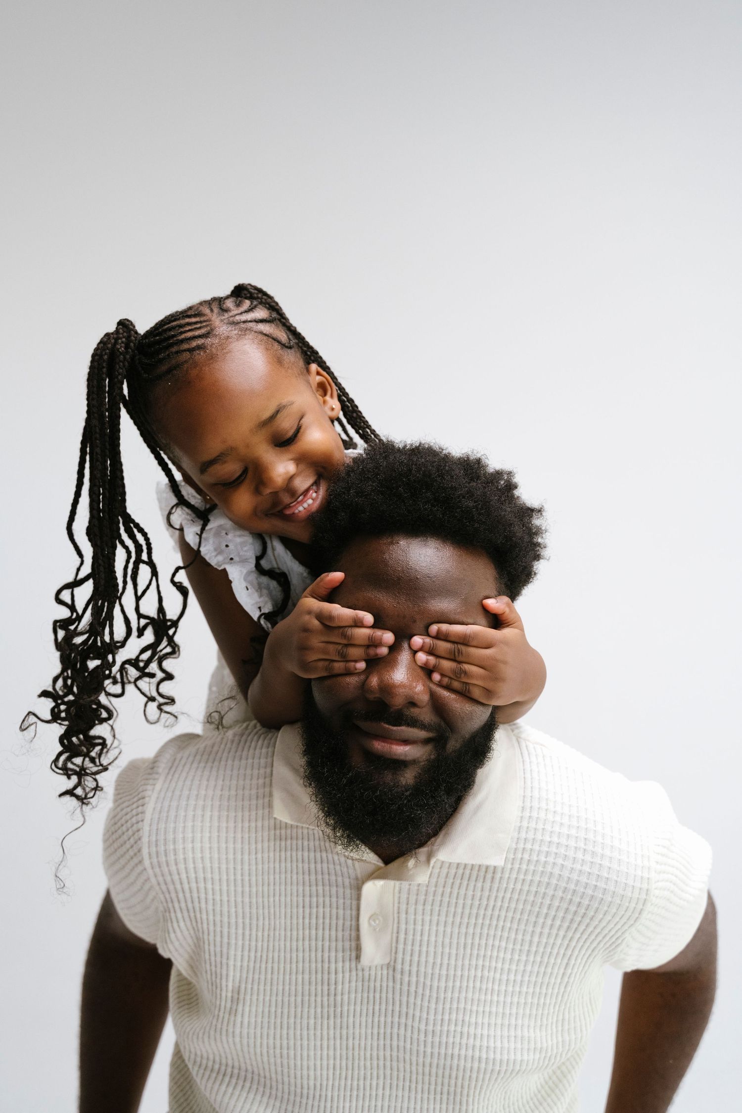 A joyful young girl covers her father's eyes from behind in a playful studio portrait.