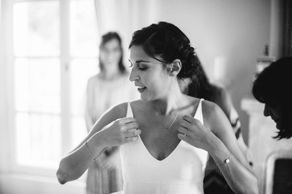 Black and white photo of bride being helped into white wedding dress by bridesmaids.