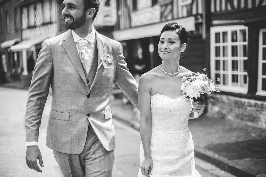 Black and white photo of bride and groom walking together on a European street lined with timber-framed buildings.