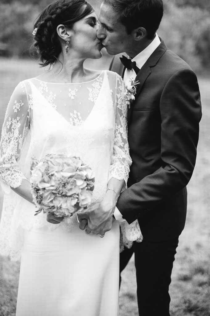 Black and white close-up of bride and groom kissing, bride holding floral bouquet.