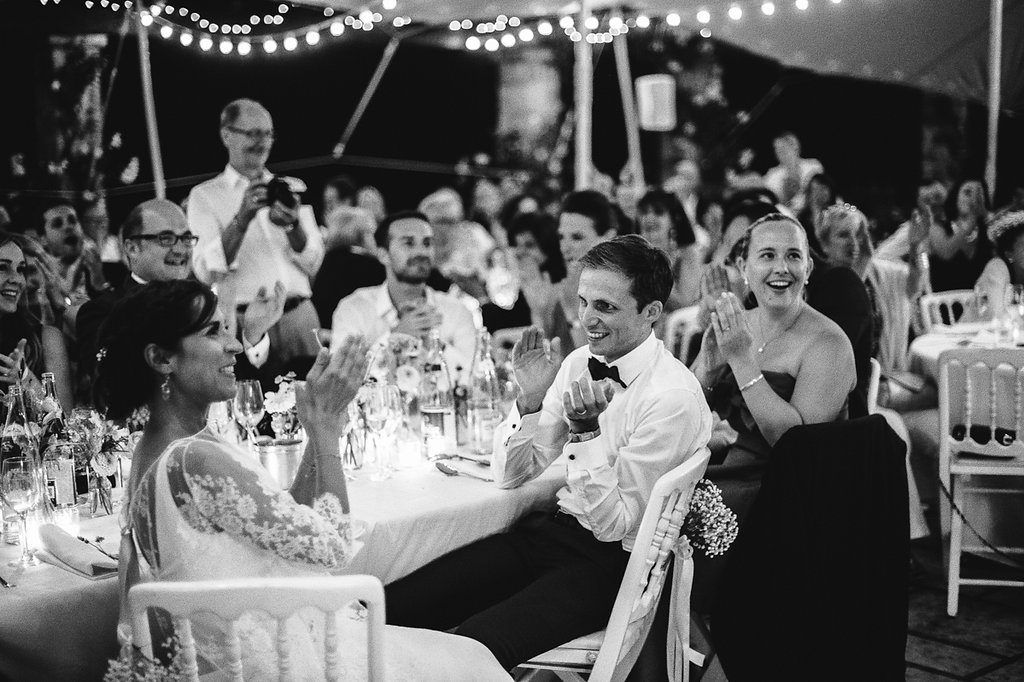 Bride and groom laughing joyfully at wedding reception table under string lights.