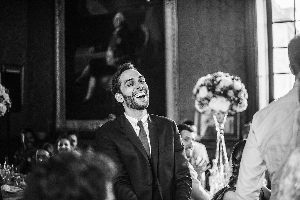 Joyful groom in black suit laughing during elegant black and white wedding reception celebration.
