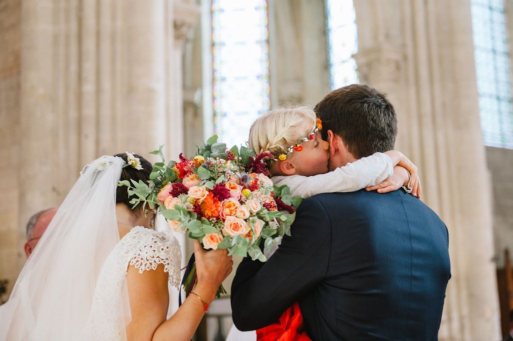 Newlyweds share a kiss behind a vibrant colorful bridal bouquet inside a historic church.