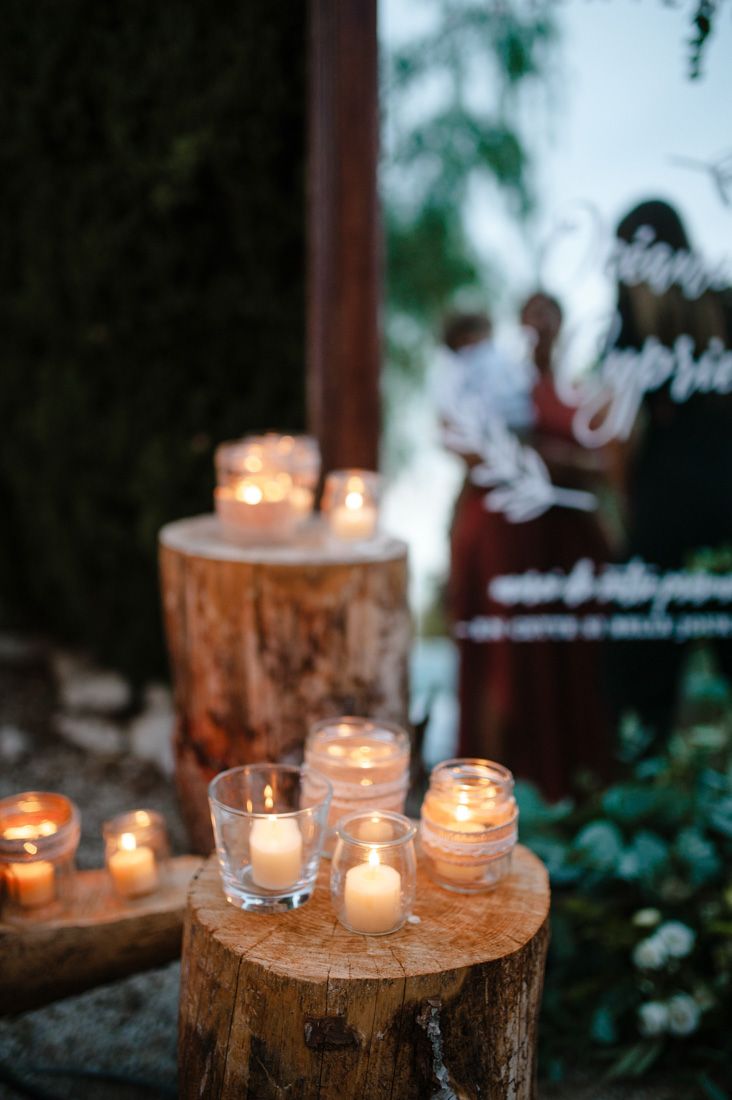 Romantic wedding decor with glowing candles on rustic wood stumps at twilight outdoor venue.