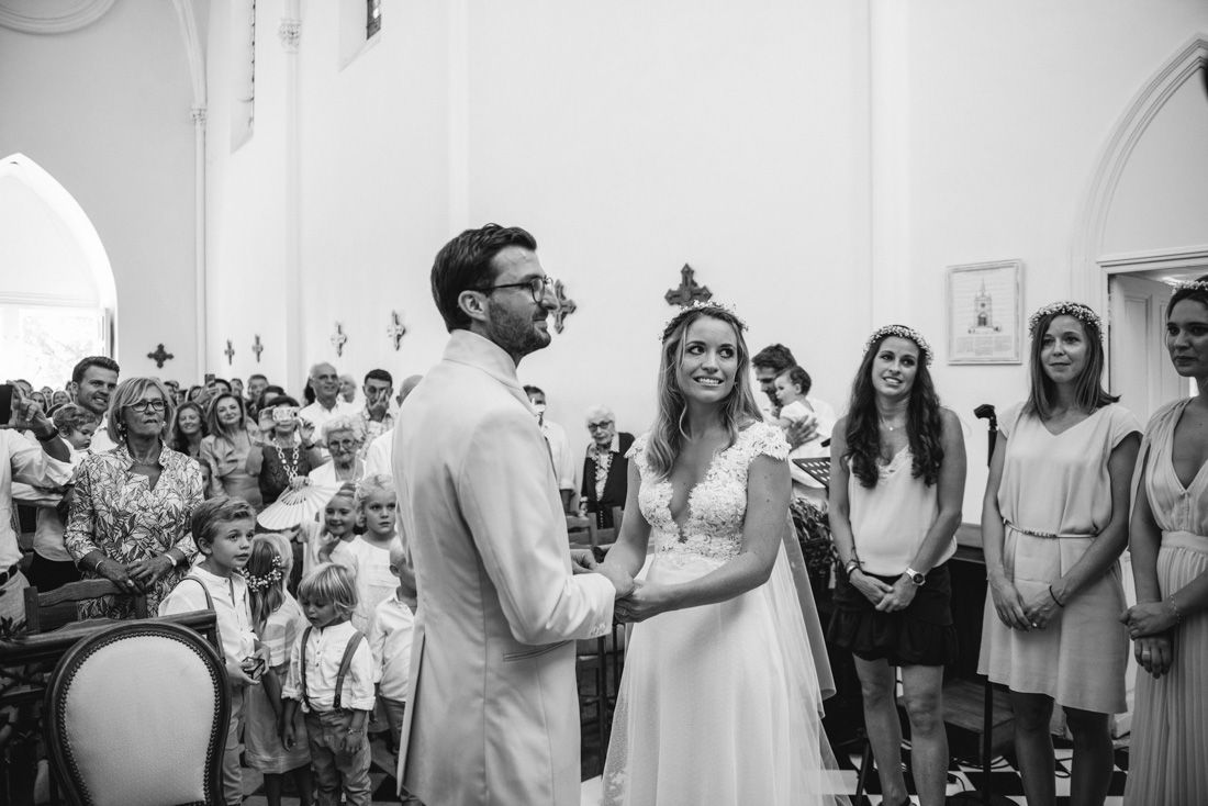 Black and white photo of a bride and groom exchanging vows at a church wedding ceremony with guests seated behind.