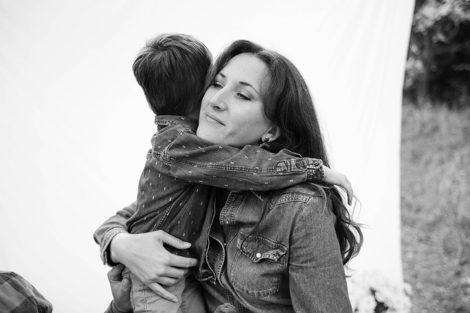 Black and white photo of a mother tenderly hugging her young child outdoors.