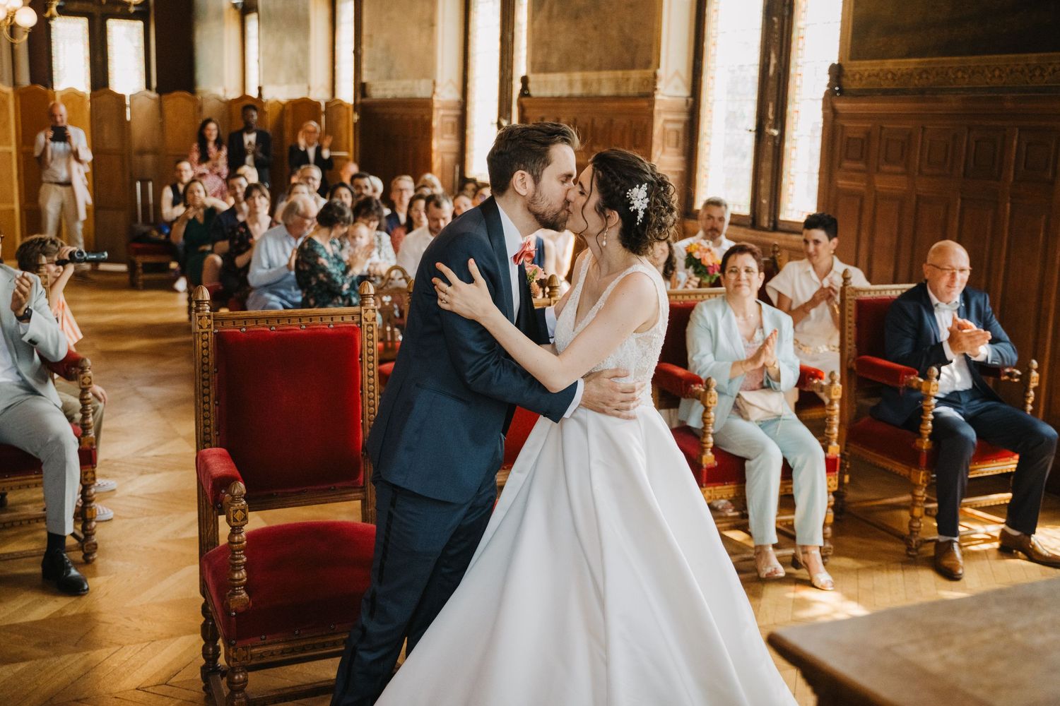 Newlyweds sharing their first kiss at the altar surrounded by applauding wedding guests.