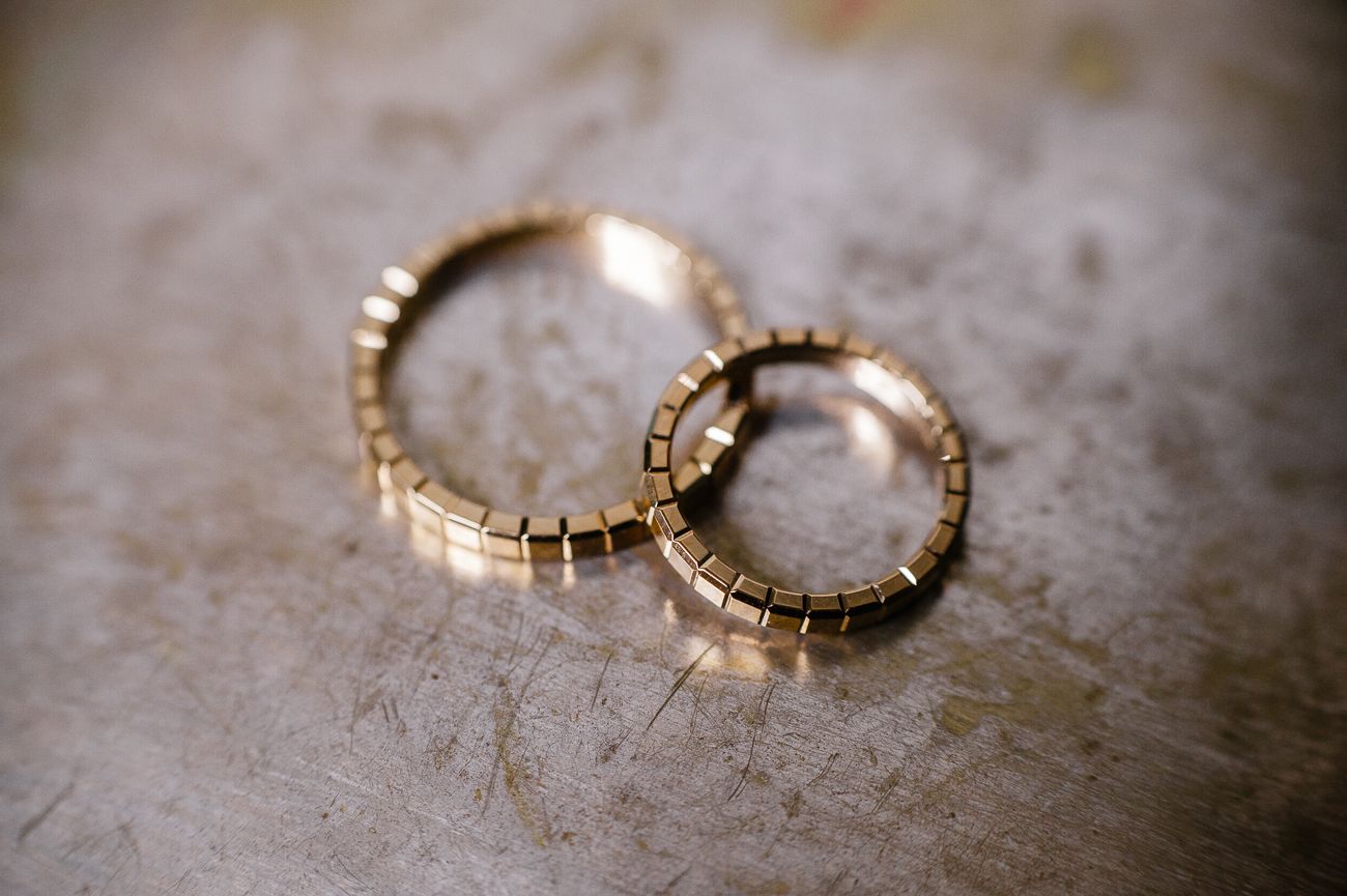 Two gold textured wedding bands with geometric pattern resting on a metallic surface.