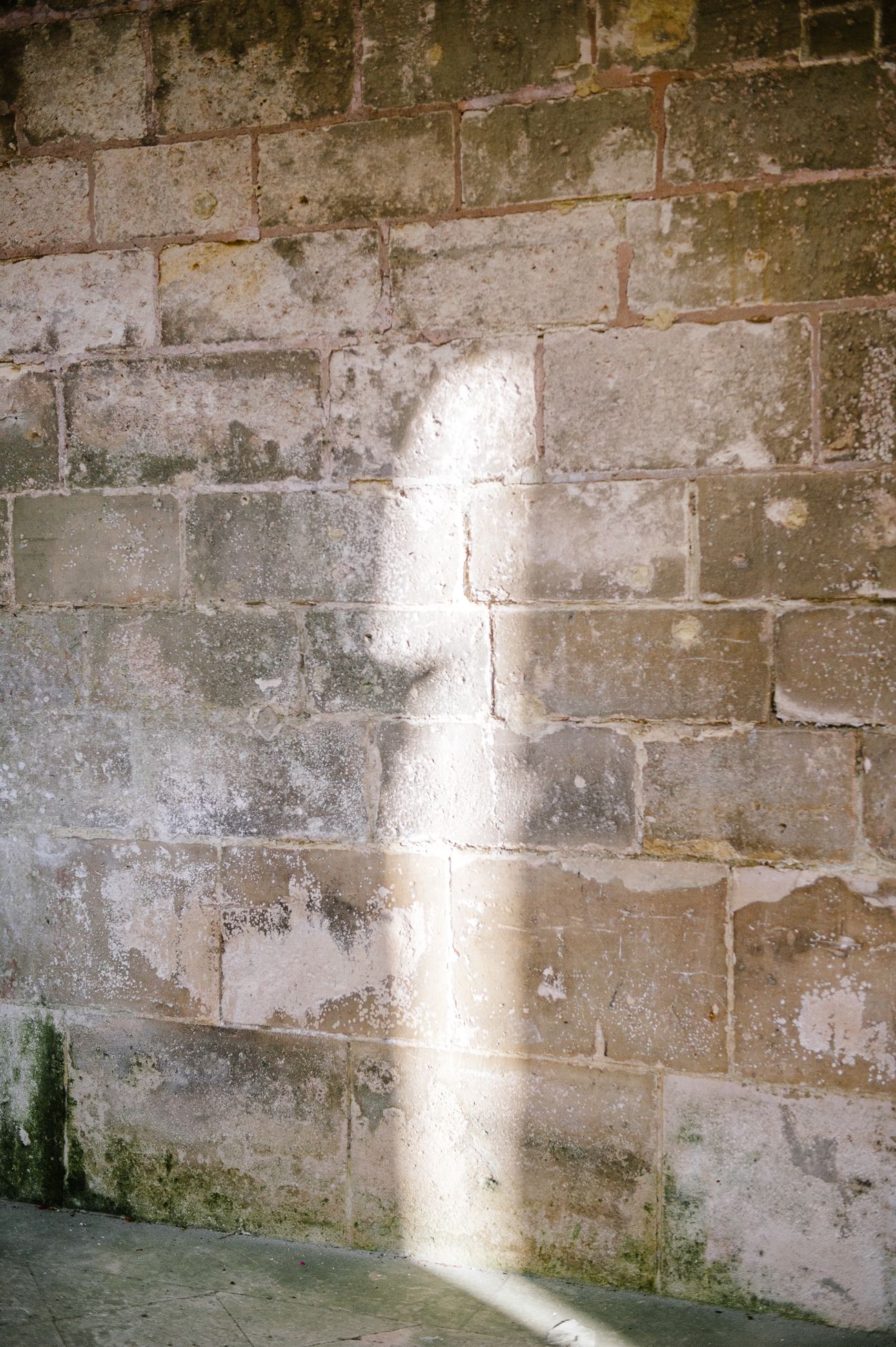 Sunlight casting a cross-shaped shadow on an aged stone brick wall with weathered texture.