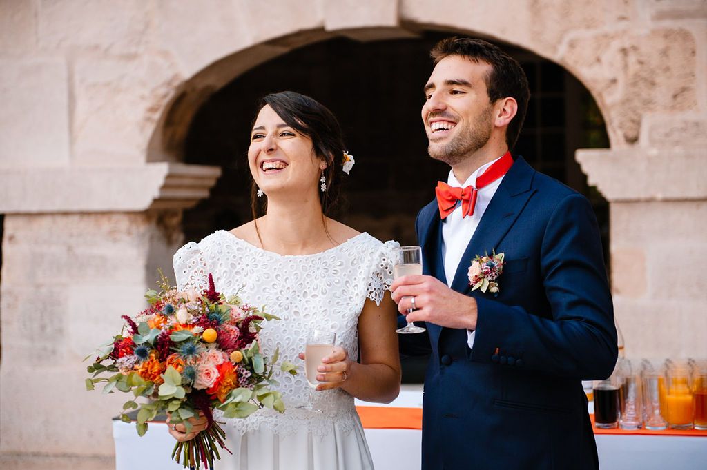 Smiling bride and groom holding champagne glasses outdoors at their wedding reception.