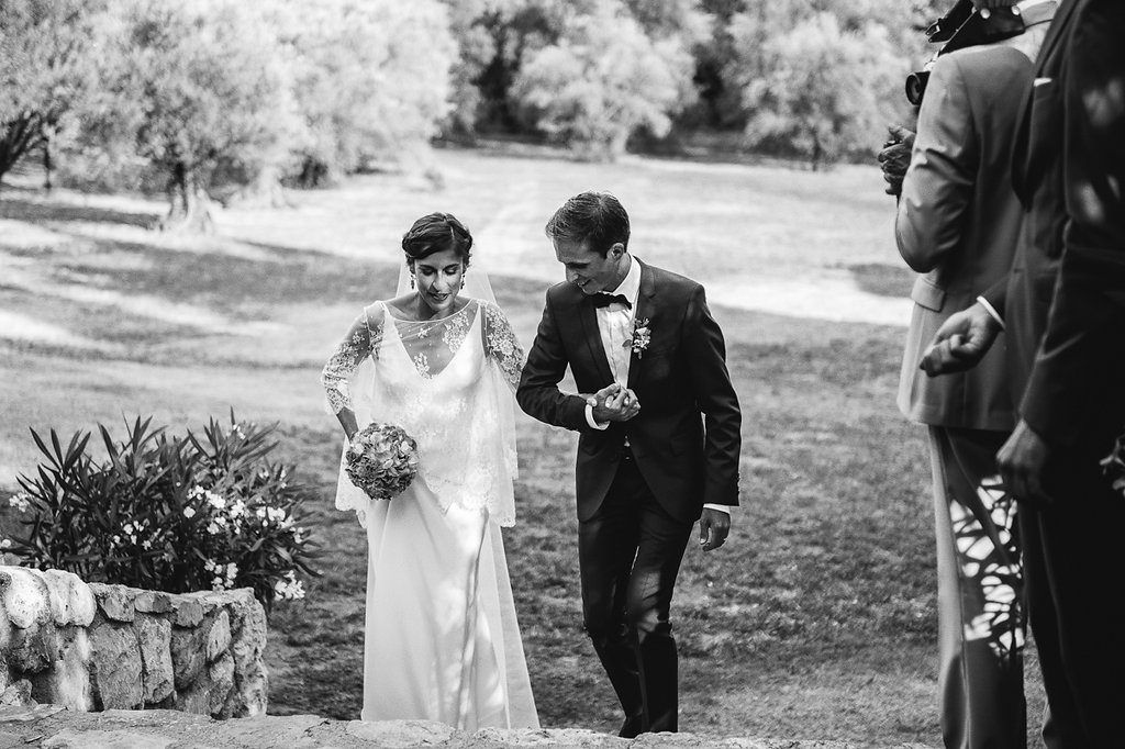 Black and white photo of bride and groom walking together during outdoor wedding ceremony in scenic garden.