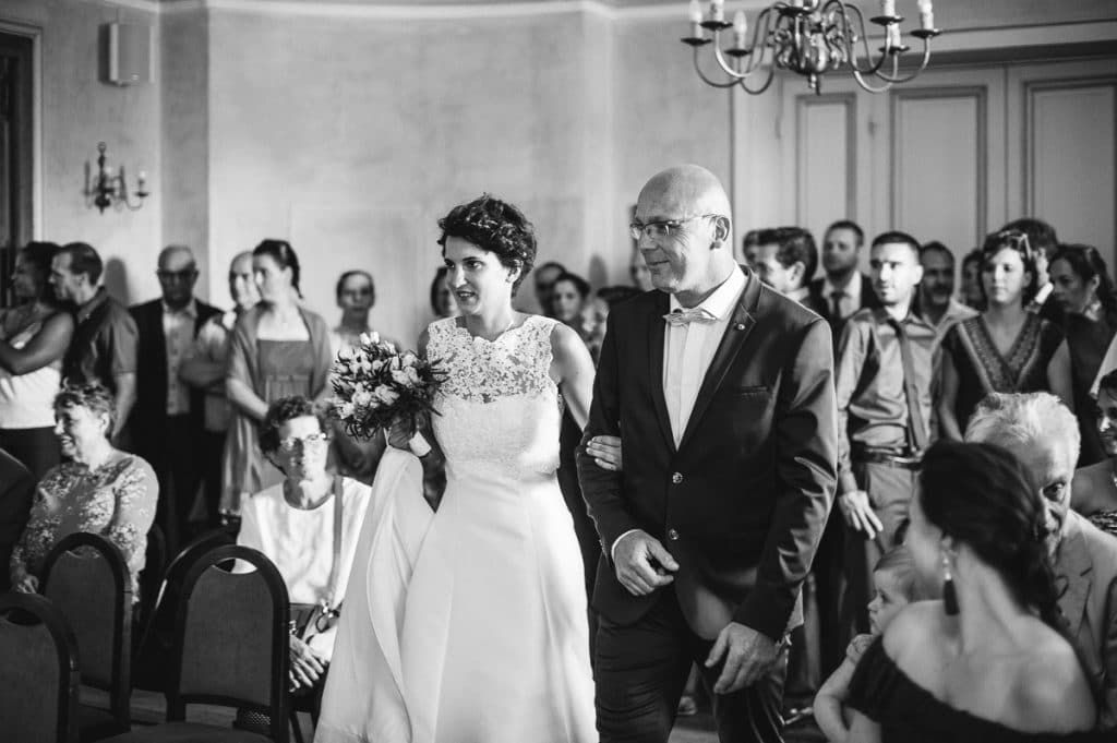 Black and white photo of a bride walking down the aisle with her escort at the ceremony.