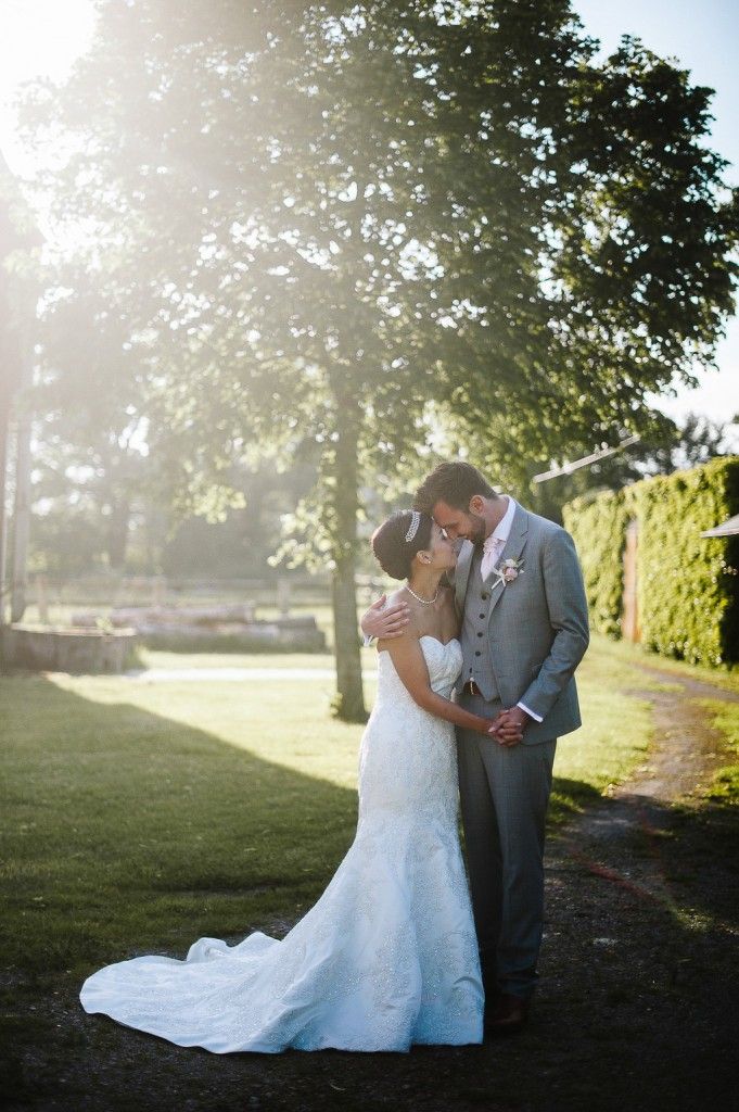 Bride and groom sharing a romantic kiss in a sunlit garden, bride wearing a lace mermaid gown.