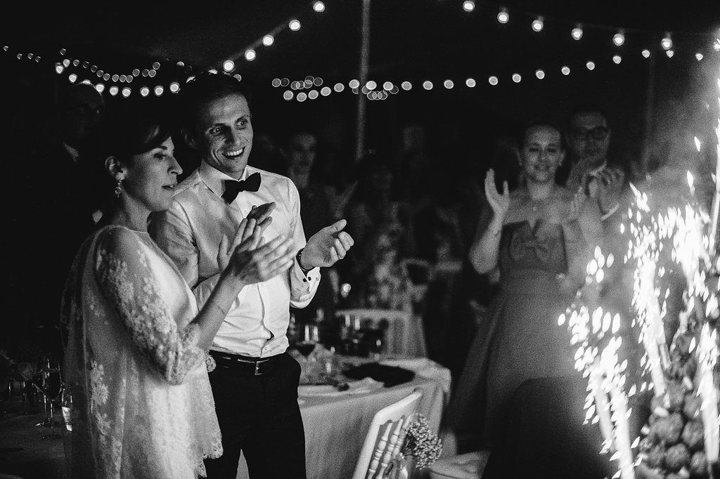 Bride and groom celebrating with sparklers at elegant outdoor wedding reception.