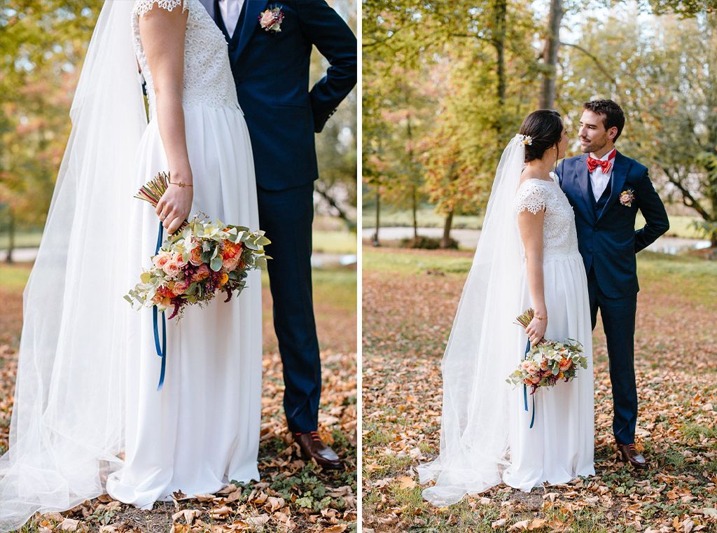 Bride holding colorful autumn bouquet stands with groom in navy suit in fall park.