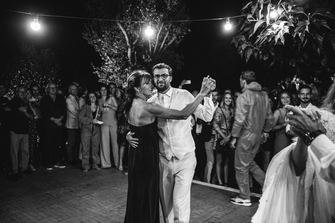 Couple shares romantic first dance outdoors at night under string lights in black and white photo.