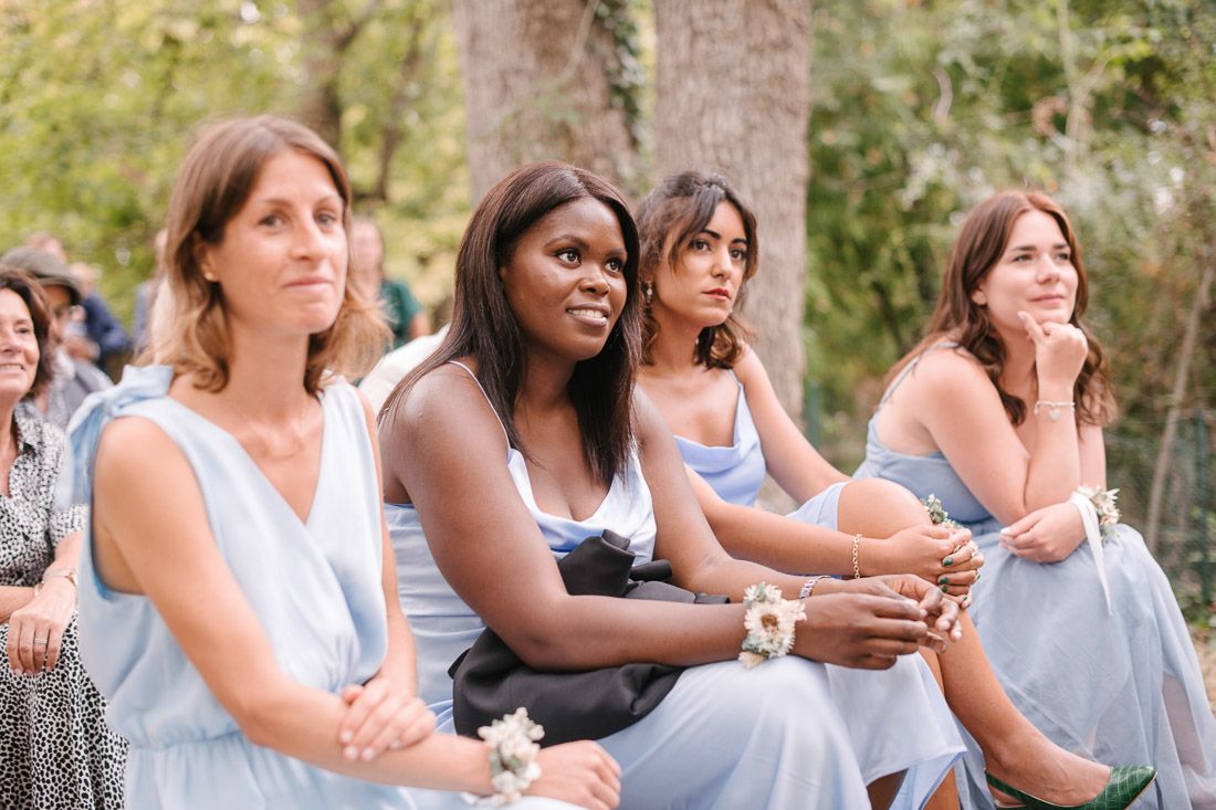 Four bridesmaids in light blue dresses seated and watching an outdoor wedding ceremony.