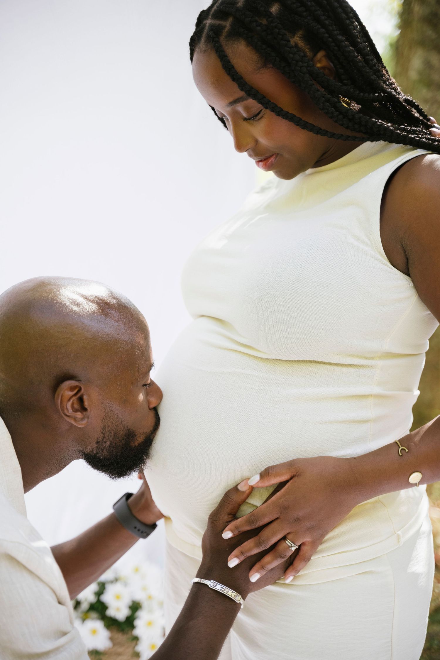 Loving man gently kissing pregnant woman's belly during outdoor maternity photoshoot.